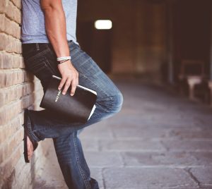 man holding Holy Bible leaning on bricked wall