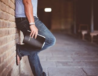 man holding Holy Bible leaning on bricked wall